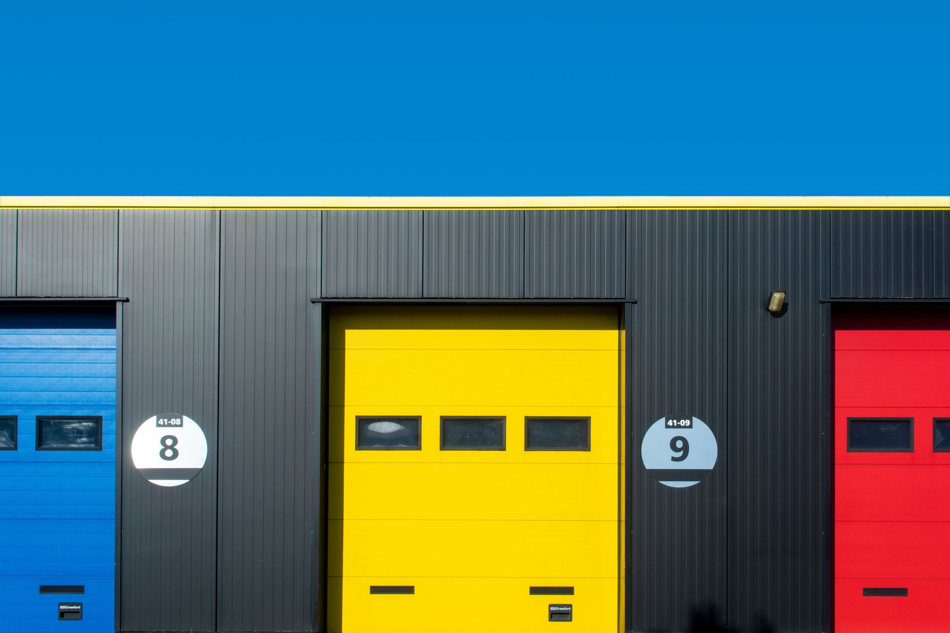 Brightly colored industrial garage doors with primary colors against a clear sky.